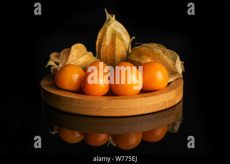 Menge ganze Frische orange Physalis symmetrisch angeordnet auf runden Bambus Untersetzer auf schwarzem Glas isoliert Stockfoto