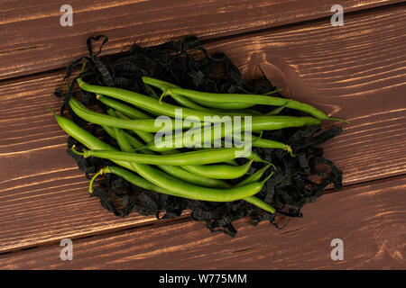 Menge ganze frische grüne Bohnen auf schwarzem krepp papier Streifen flatlay auf braunem Holz Stockfoto