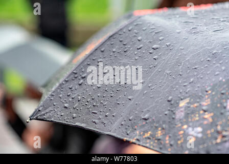 Tag Regen, starker Regen in der Stadt, fällt auf der Oberfläche des schwarzen Regenschirm, Menschen mit Sonnenschirmen während Sturm Stockfoto