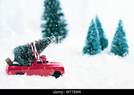 Eine 1950er antike Vintage rot Spielzeug-LKW schleppen einen Weihnachtsbaum nach Hause durch einen verschneiten Winter Wonder Land. Selektiver Fokus auf Fahrzeug mit hinterg verschwommen Stockfoto