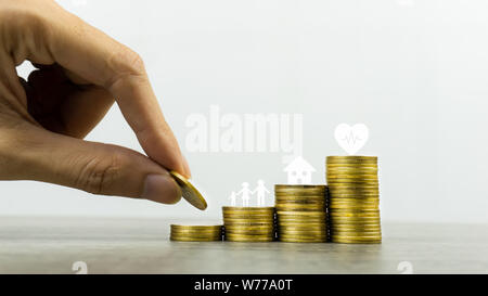 Speichern oder das Geld für die Familie in Zukunft Konzept. Ein Mann Hand Münze in steigenden Stapel von Münzen mit Herz, Familie und kleines Haus Modell Stockfoto