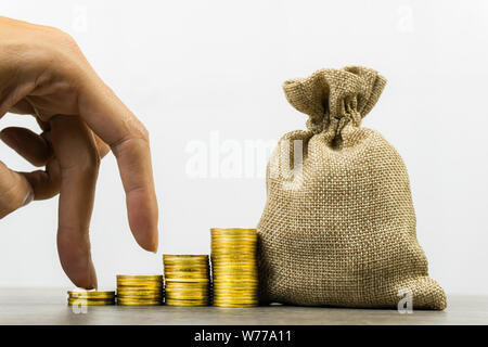 Spart Geld. Geld Investitionen. Ein Geschäftsmann Hand auf der Münzen mit Geld Beutel auf Holz Tisch Stapel auf weißem Hintergrund. Zeigt langfristige Investition t Stockfoto