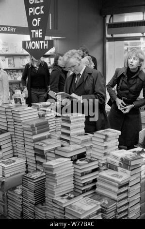 1970er beschäftigt überfüllten Buchladen Menschen Browsen, Einkaufen Kauf Entscheidung, welches Buch zu kaufen. Pick des Monats Stapel von Büchern. Hoch gestapelt. 70ER JAHRE UK HOMER SYKES Stockfoto