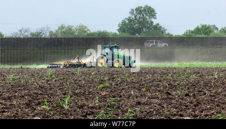 Eine Zoll- und Grenzschutz Agent Fahrzeug Patrouillen der Grenzmauer in der Nähe von Brownsville, Texas, während ein Bauer sein Feld pflügen. Stockfoto