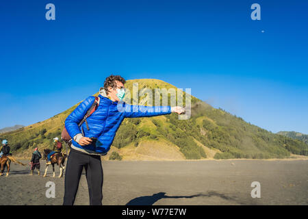 Junger Mann touristische berührt vulkanischen Sand in der Bromo Tengger Semeru National Park auf der Insel Java, Indonesien. Er genießt einen herrlichen Blick auf den Stockfoto