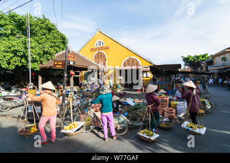 Hoi An, Vietnam - Juni 2019: Straße Obst Anbieter wandern durch bunte Markt Gebäude in der Altstadt. Stockfoto