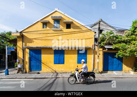 Hoi An, Vietnam - Juni 2019: Mann, Jahrgang scooter neben bunten Haus in der Altstadt Stockfoto