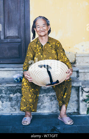 Hoi An, Vietnam - Juni 2019: Porträt der alten vietnamesischen Frau mit traditionellen konischen Hut und lächelnd Stockfoto