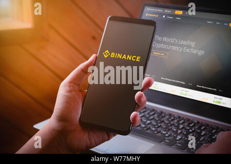 Bangkok, Thailand - August 5, 2019: Hände halten Smartphone mit binance Logo auf dem Bildschirm und binance Website auf Laptop Hintergrund. Binance ist ein Leadin Stockfoto