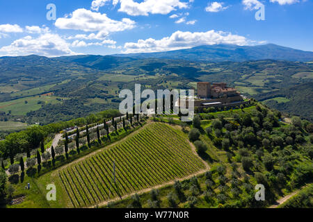 Eine Burg steht auf einem toskanischen Hügel von Zypressen umgeben. Berge prägen die Landschaft im Hintergrund. Stockfoto