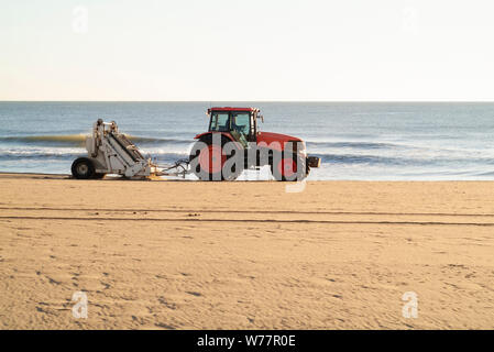 MORGENFEGEN: Ein Traktor mit angeschlossenem Sieb reinigt und entfernt in den frühen Morgenstunden Müll vom Strand von Virginia. Stockfoto