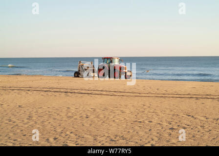 MORGENFEGEN: Ein Traktor mit angeschlossenem Sieb reinigt und entfernt in den frühen Morgenstunden Müll vom Strand von Virginia. Stockfoto