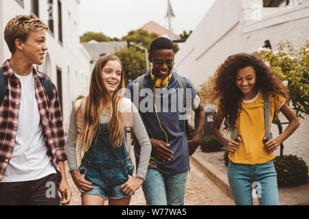Gruppe von Multiethnischen college Freunde zu Fuß auf der Straße. Smiling teenage Freunde tragen College Taschen wandern im Freien und zu reden. Stockfoto