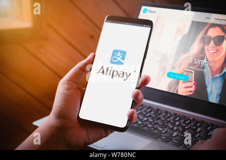 Bangkok, Thailand - August 5, 2019: Hände halten Smartphone mit alipay Logo auf dem Bildschirm und Alipay website auf Laptop Hintergrund. Alipay ist mobil und Stockfoto