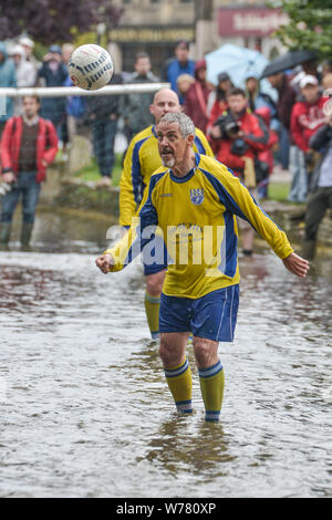 Eine britische Tradition, River Football in Bourton-on-the-Water, Cotswolds August 2015. Das Spiel findet jeden August an Feiertagen statt. Das Spiel ist ein fünf-ein-Seite-Fußballspiel, aber in der Fluss Windrush, die durch die Stadt läuft. Bewohner und Besucher säumen den Rand des Wassers und Brücken, um die besten Plätze zu bekommen, aber riskieren Sie ein Bad zu bekommen, wenn das Geschehen zu nahe kommt. 2015 nahm der britische Prominent Griff Rhys Jones an den Dreharbeiten für EIN großes britisches Abenteuer Teil. Kredit: Michael Scott/Alamy Live News Stockfoto