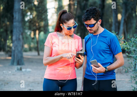 Kaukasische Paar beobachten mobile Anwendung und Ausübung in einem Park. Gesundes Leben Konzept Stockfoto