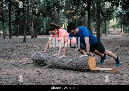 Paar tun Push-ups auf einem Baumstamm in einem Park Stockfoto