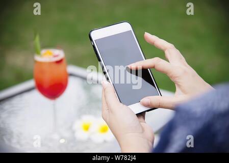 Dame mit Handy im grünen Garten entspannen Sie sich mit einem alkoholfreien Getränk Hintergrund - Mensch und Technik lifestyle Konzept Stockfoto