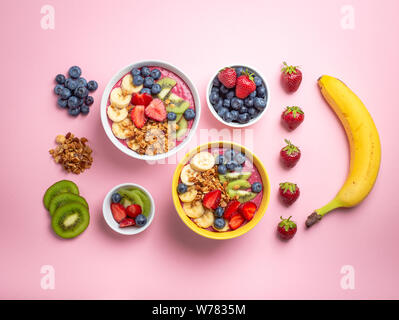 Kochen acai Smoothie Schüssel. Zutaten für einen frischen Smoothie Schüssel: frische Erdbeeren, Banane, Heidelbeeren, Kiwi Obst und Müsli auf Pastell rosa Stockfoto