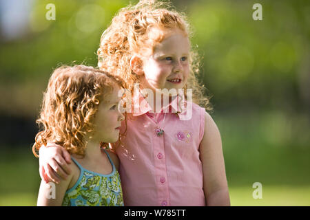 Junges Mädchen mit ihren Arm um ihre jüngere Schwester draußen in der Sonne. Stockfoto