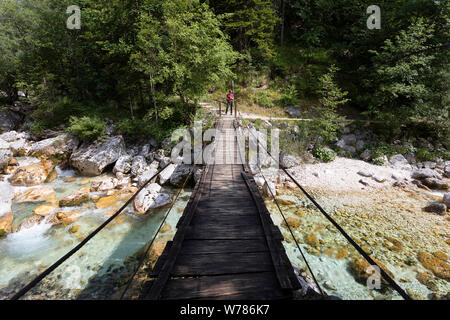 Frau Kreuzung eine hölzerne Hängebrücke über schöne türkisblaue Fluss Soca während Trekking auf dem Trail, Bovec Soca, Slowenien, Europa Stockfoto