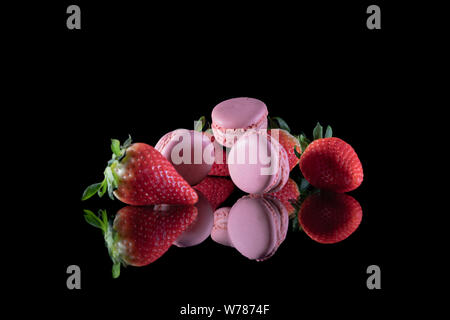 Erdbeeren und leckere Makronen auf einem Glastisch mit einem schwarzen Hintergrund gestapelt - Close-up Stockfoto