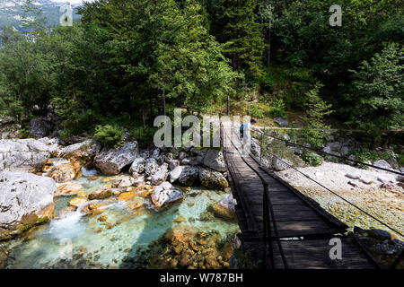 Junge Kreuzung eine hölzerne Hängebrücke über schöne türkisblaue Fluss Soca während Trekking auf dem Trail, Bovec Soca, Slowenien, Europa Stockfoto