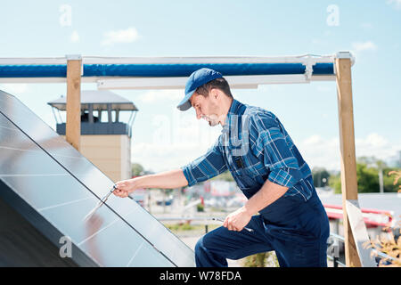 Junge Techniker Meister in Arbeitskleidung biegen über Solarzellen auf dem Dach Stockfoto