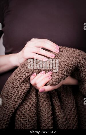 Schöne weibliche Hände halten Braun gestrickte Pullover. Maniküre mit rosa Nagellack. Gemütliche Konzept Stockfoto