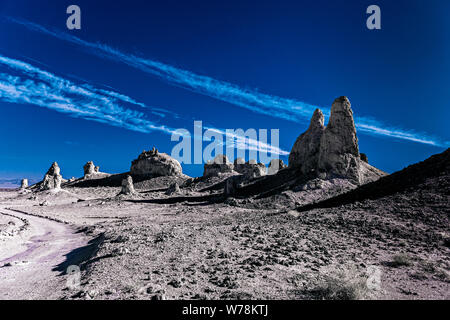 Schmutz der Straße durch die öden kargen Wüstenlandschaft mit Zinnen und Felsformationen in Schwarz und Weiß unter blauem Himmel mit weißen Wolken. Stockfoto