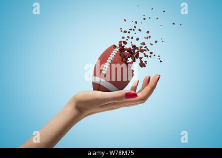 Weibliche Hand, die American football Ball zerbricht in Stücke auf blauem Hintergrund. Digitale Kunst Aktivitäten im Freien. Sportartikel. Stockfoto
