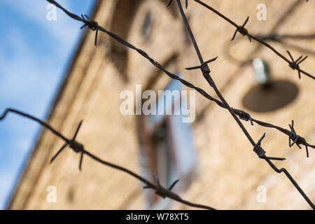 Nahaufnahme einer verrosteten Stacheldrahtzaun rund um einen Konzentrations- und Vernichtungslager, alte Baracke mit Fenster und Lampe in Soft Focus Stockfoto