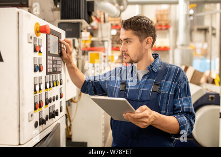 Junge Ingenieur die Kontrolle der Angaben auf dem Bedienfeld während Einstellung der Parameter Stockfoto