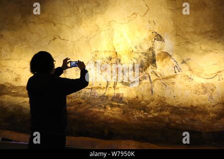 Ein Besucher nimmt Fotos der "Panel der Schwarze Kuh'' zeigt eine schwarze Kuh, die von einer Gruppe von Pferden, einer der Replik Höhlenmalereien von Lascaux auf d Stockfoto