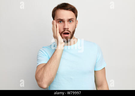 Aufgeregt beeindruckt Mann mit einem Palm auf seiner Wange schockiert, Mund in der Überraschung geöffnet. nach oben Porträt schließen. isoliert weißer Hintergrund. Studio erschossen. Gesichts exp Stockfoto