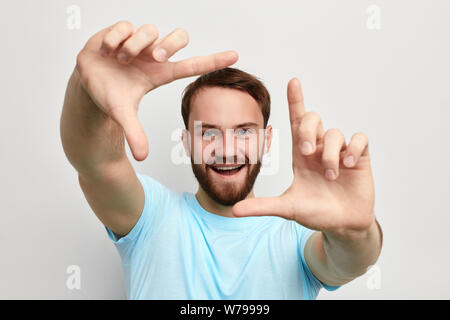 Happy fröhlich aussehenden Mann, der Rahmen mit seinen Händen, Kamera und lächelnd, stehend gegen isoliert weißer Hintergrund. studio Shot Stockfoto
