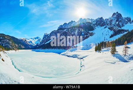 Winter Panorama der Gosausee, mit Eis bedeckt und durch verschneite Pisten von Dachstein Alpen mit üppigen Nadelwäldern und felsigen Gipfeln umgeben, Gosau, Stockfoto