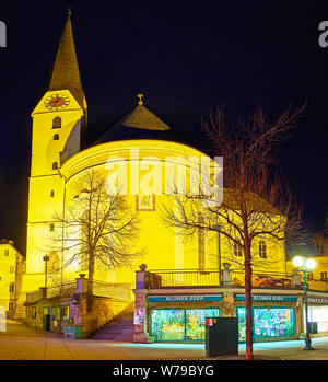 BAD ISCHL, Österreich - 20. FEBRUAR 2019: Die Apsis und hohen Glockenturm von St. Nikolaus Pfarrkirche in Abend Leuchten mit Blumenladen auf der foregrou Stockfoto