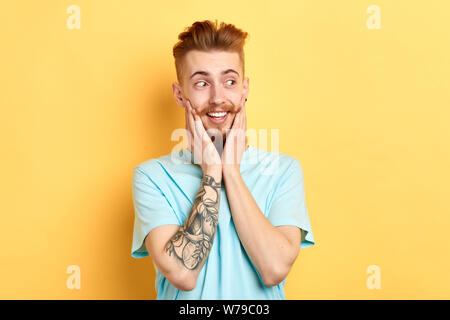 Fasziniert aufgeregt Mann mit Tattoo auf dem Arm halten Palmen auf Wangen, beiseite suchen, eine tolle Idee, Plan, Träumen, neues Auto, neue Frisur. cl Stockfoto