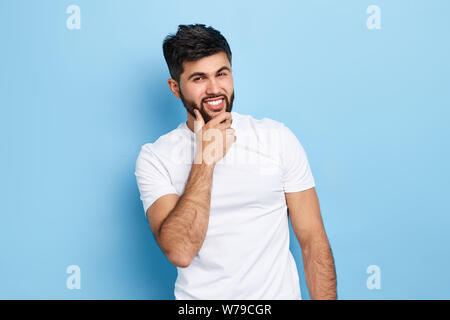 Bärtige fröhlicher Kerl sein Kinn berühren und Blick in die Kamera. nach oben Porträt schließen, isolierte blauen Hintergrund, Studio erschossen. macho Flirten mit Frauen. Stockfoto