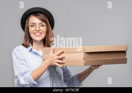 Happy girl in Hut, T-Shirt und Brillen Holding von dünnen Kartonverpackungen Stapel Stockfoto