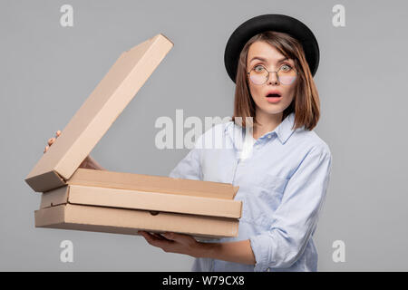 Erstaunt junge Frau in casualwear Eröffnung einer der Kartons Stockfoto