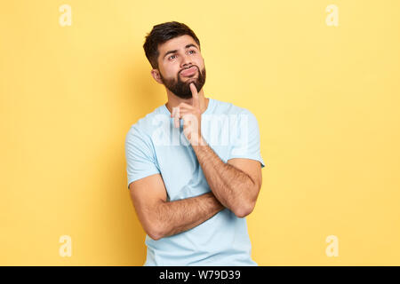 Gut aussehenden Mann mit dem Finger auf seinem Kinn bis suchen, isolierte blauen Hintergrund, Studio erschossen. Idee, Plan des Geschäfts Stockfoto