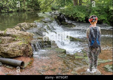 Junge beobachtet einen sanften Wasserfall bei Clumber Park, Nottinghamshire, Großbritannien Stockfoto