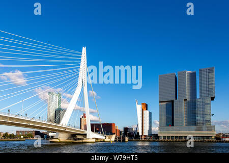 Hohe Gebäude im Finanzdistrikt und Hafen mit der Erasmus Brücke aus dem Wasser gegen einen blauen Himmel mit Fluffy Clouds gesehen Stockfoto