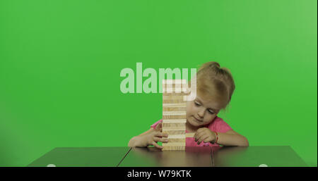 Das Kind spielt den Jenga. Ein kleines Mädchen, zieht die holzklötze von einem Turm. Block Ausbau Spiel. Chroma Key Hintergrund Stockfoto