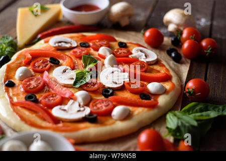 - Aus der Nähe Pizza mit Mozzarella, Oliven, Champignons, Tomaten, Paprika und Kräuter vor dem Backen Stockfoto