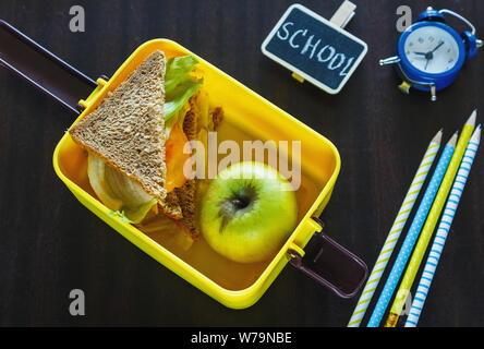 Schule gelb Lunch Box mit Sandwich, grüner Apfel, am schwarzen Brett. Gesunde Ernährung in der Schule. Zurück zu Hintergrund Schule. Flach, Ansicht von oben. Stockfoto