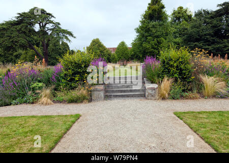 Sommergarten mit Stein weg zu einer Treppe zu Wilde Blumenwiese, von alten Bäumen umgeben. Stockfoto