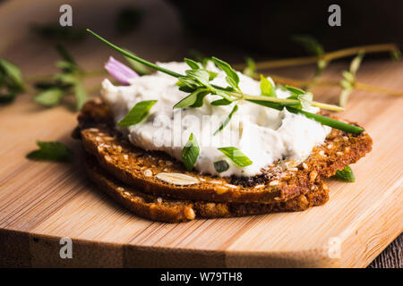 Eine köstliche Knoblauch und Schnittlauch Frischkäse auf herbed Cracker auf einem Bambus Schneidebrett gestapelt. Stockfoto